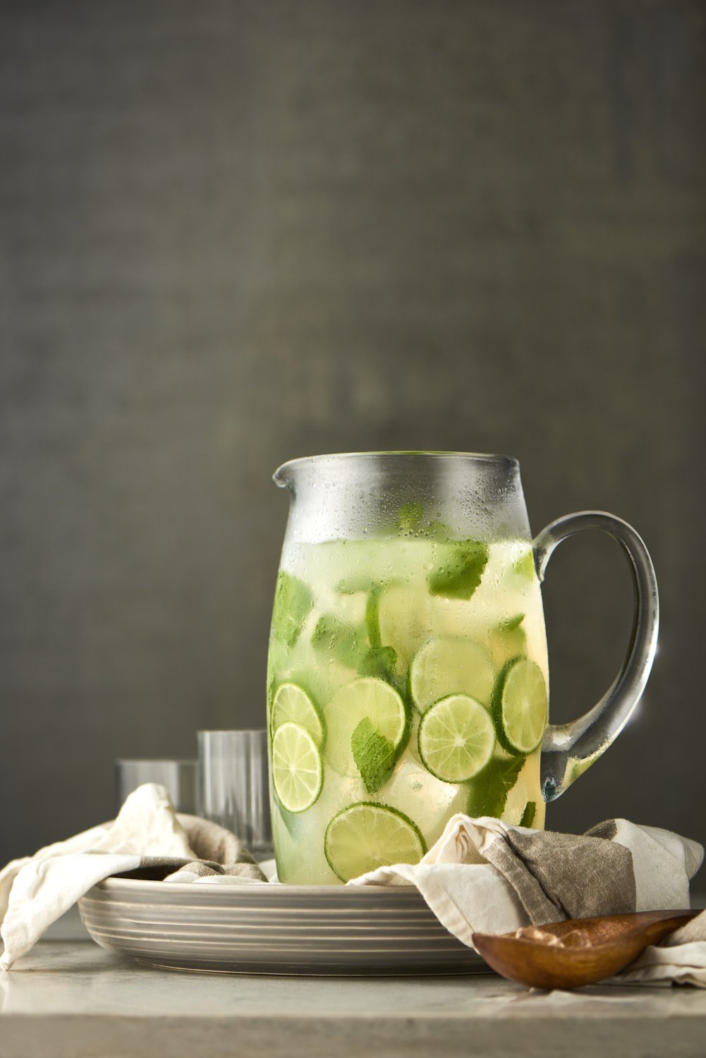 Pitcher of mojito with ice on a rustic wooden surface, soft natural light and a clean casual wellness drink aesthetic