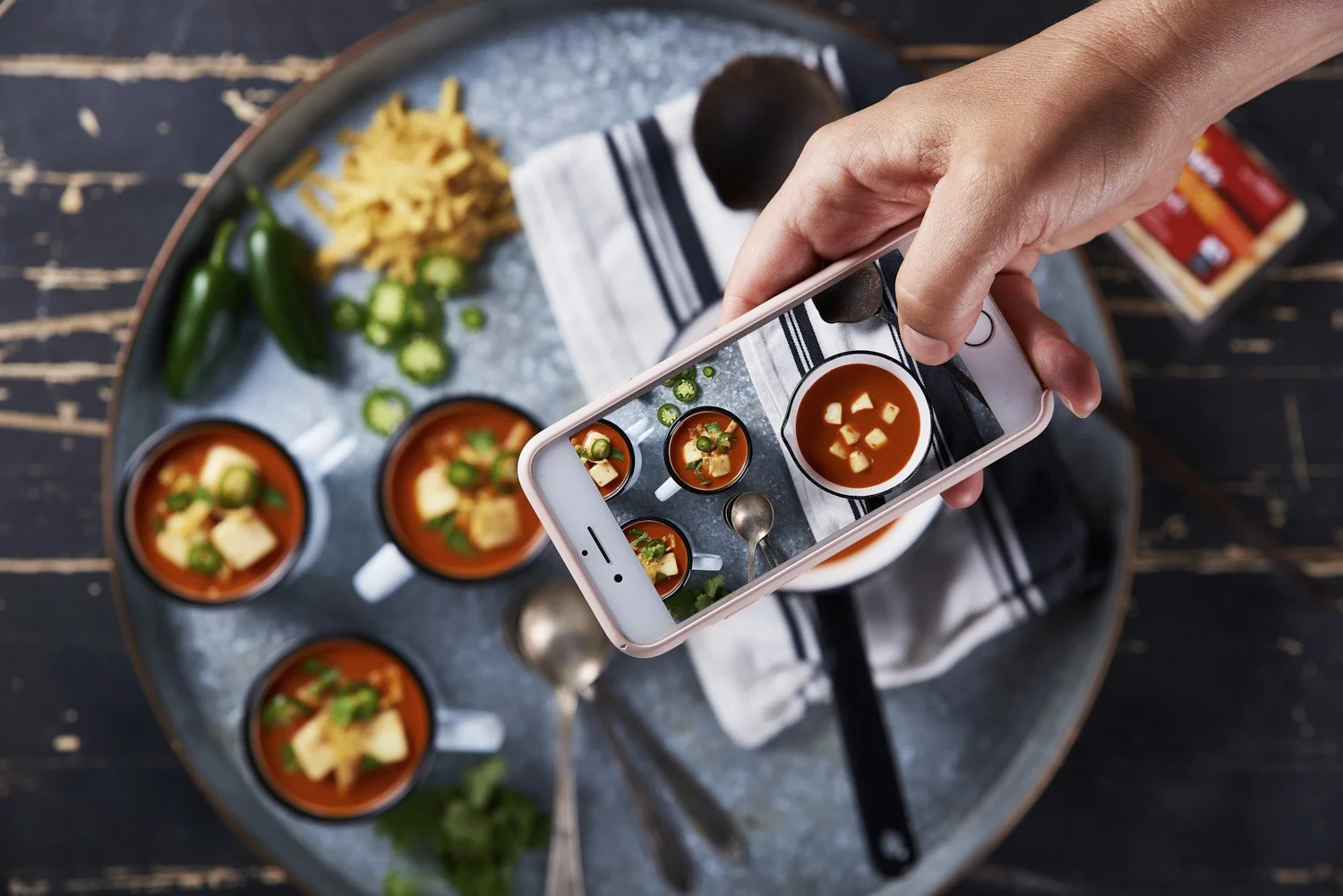 Action overhead shot of two hands using a ladle to fill a muffin tin with colorful vegetable batter on a dark stovetop or prep surface