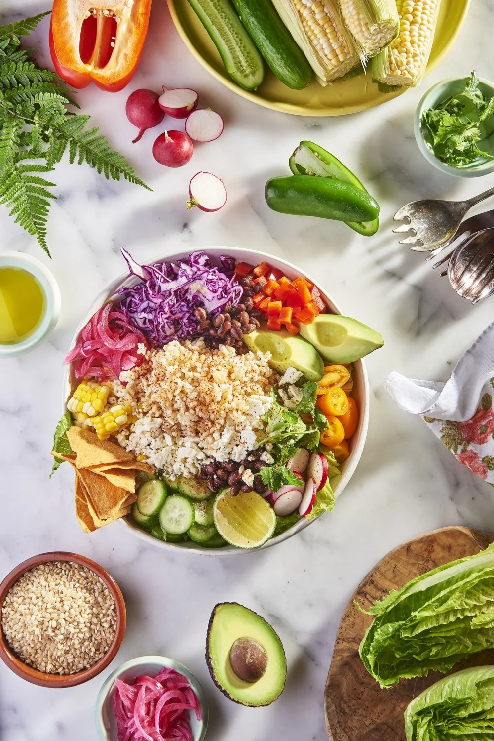 Vibrant rice bowl topped with sliced avocado, shredded purple cabbage, fresh herbs, sesame seeds, and colorful garnishes, shot from above on a light surface