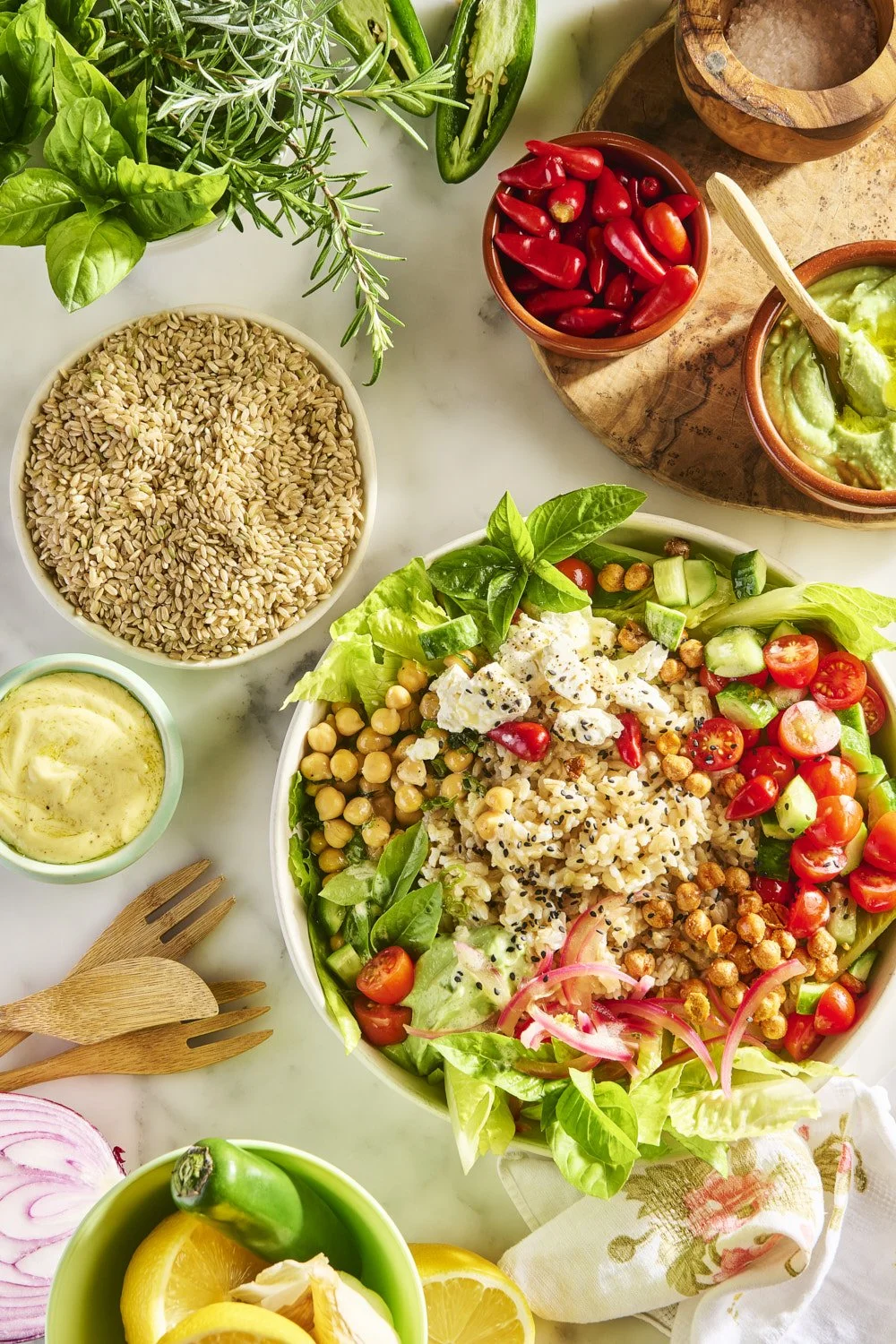 Overhead flat lay of a vibrant grain bowl with lentils, pomegranate seeds, fresh parsley, and sliced vegetables arranged on a marble surface