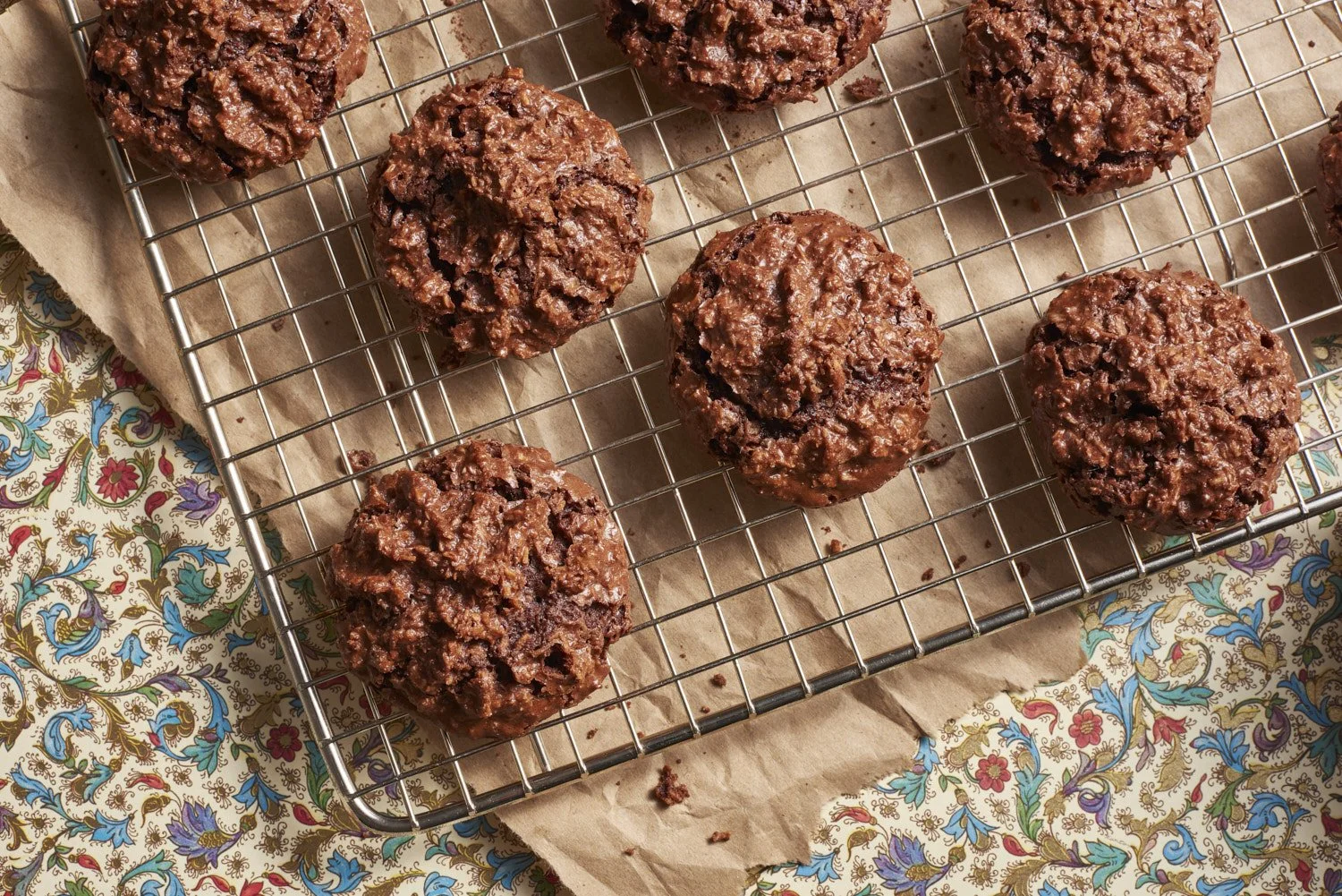 Freshly baked chocolate crinkle cookies arranged on a wire cooling rack, set on a folded red and white linen cloth with a dusting of powdered sugar