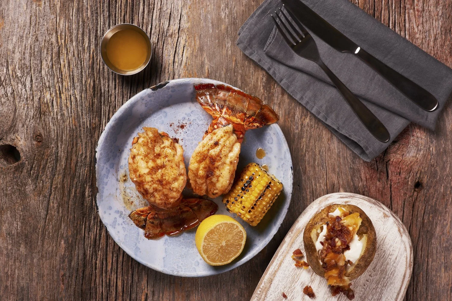  Overhead flat lay of lobster filet mignon surf and turf, plated on a rustic ceramic dish with dark cutlery on the side
