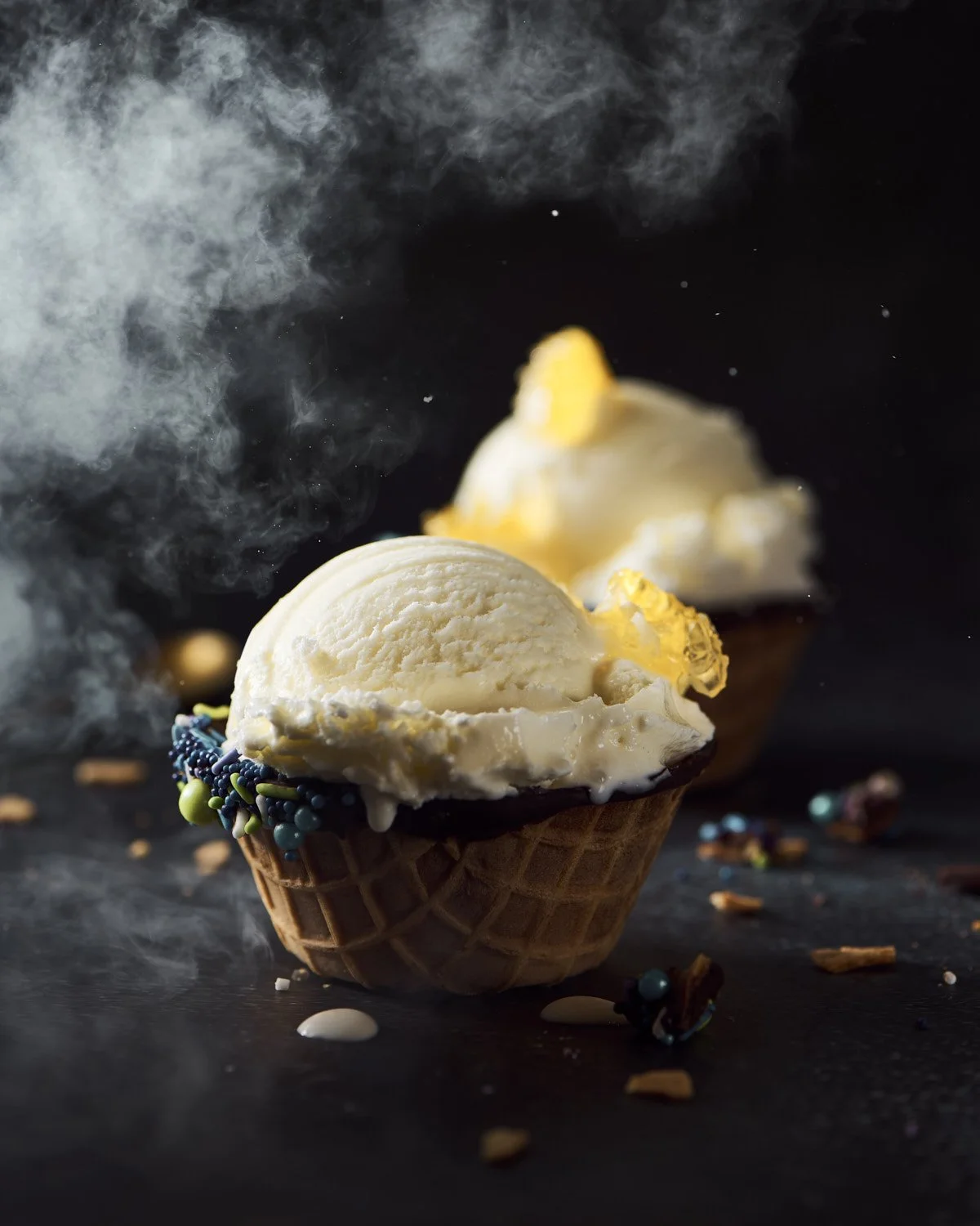 ark dramatic studio shot of a frosted ice cream bowl topped with a scoop of vanilla ice cream, dry ice smoke swirling around the base on black background