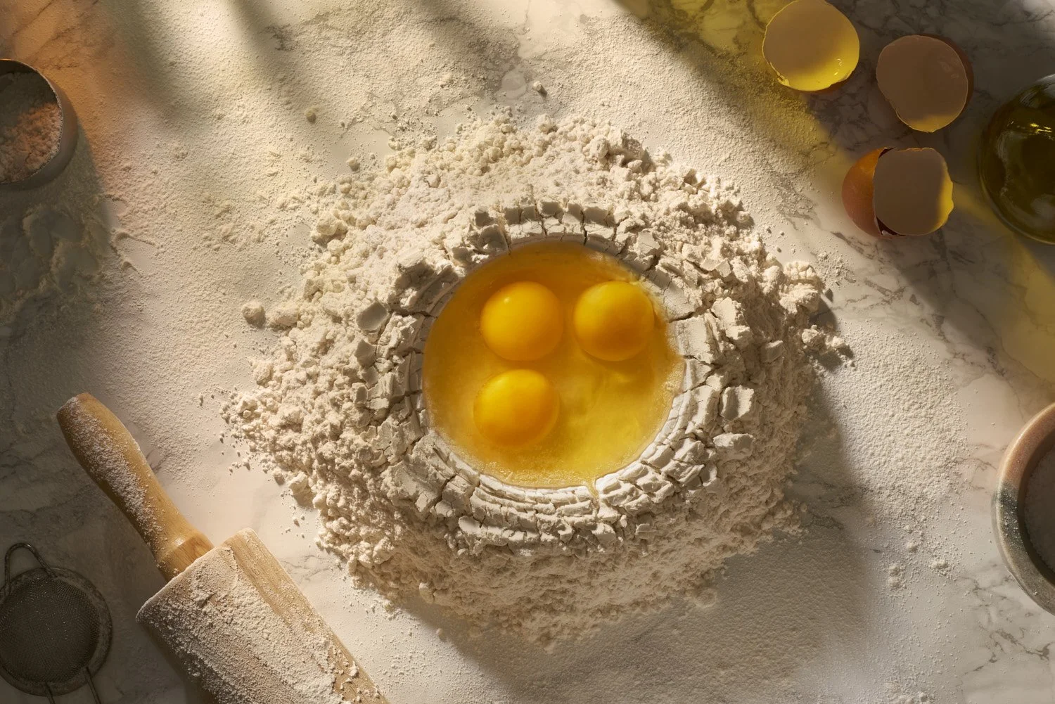 Close-up of a raw egg cracked into a well formed in a mound of flour on a dusted wooden surface, soft natural light from above