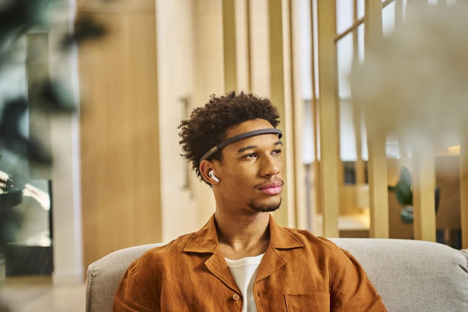 Young Black man seated in a modern warmly lit room wearing a tech headband wearable, looking to one side, lifestyle portrait with natural ambient light