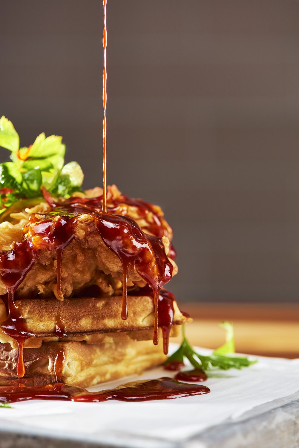 Extreme close-up of a chicken and waffle sandwich on a white plate with glossy dripping sauce