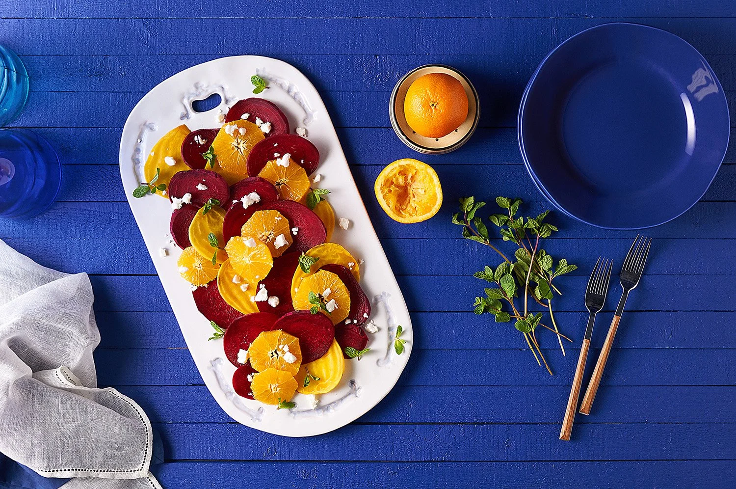 Roasted beets and oranges
 with fresh herbs and microgreens served on a white oval dish, placed on a bold royal blue surface