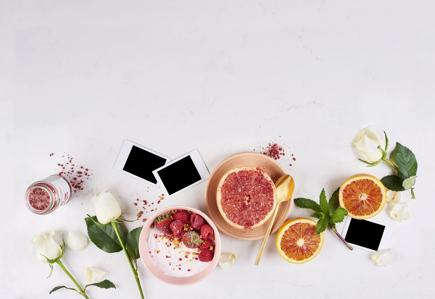 Minimal flat lay of sliced fresh figs, small flowers, and delicate leaves arranged loosely on a clean marble background with soft natural even lighting