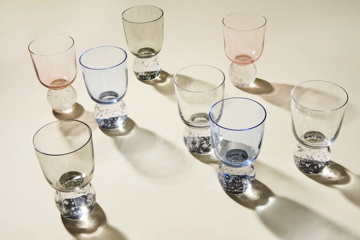Flat lay of multiple clear glass tumblers and rocks glasses arranged at angles on a light marble surface with soft directional shadow play