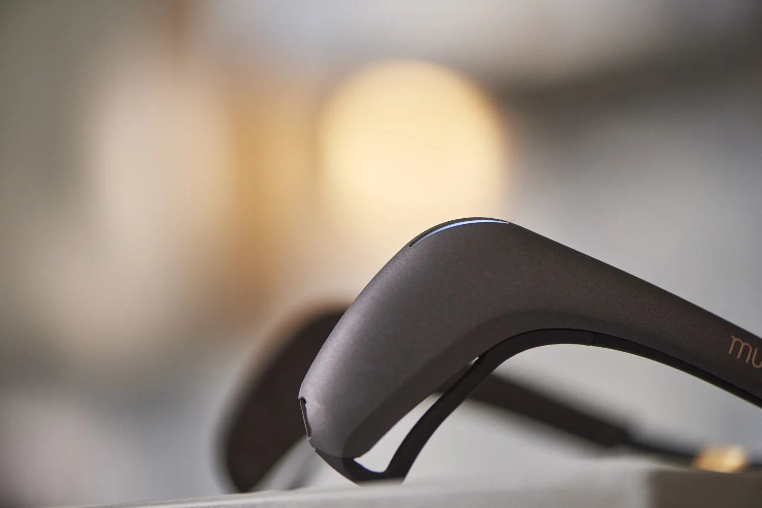 Close-up detail shot of a dark grey curved tech wearable headband, shallow depth of field with soft bokeh background emphasizing product form and material texture