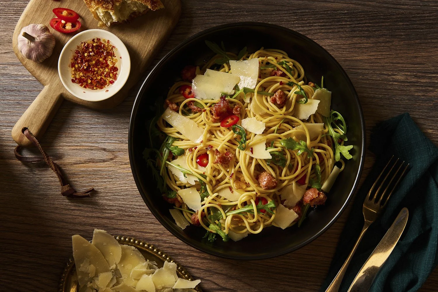 spaghetti with shredded vegetables, fresh herbs, and chili flakes in a dark skillet, warm directional lighting creating rich golden and amber tones