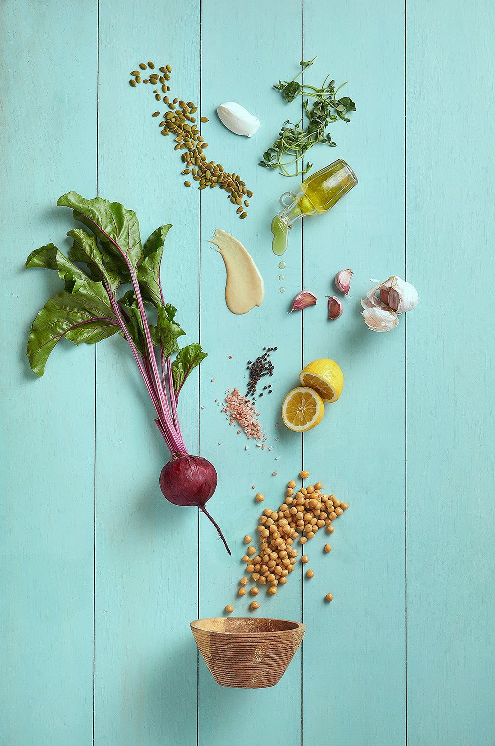 Deconstructed vegetable and grain bowl with ingredients scattered artfully including beets, radishes, and greens, photographed flat lay on a bright teal blue background
