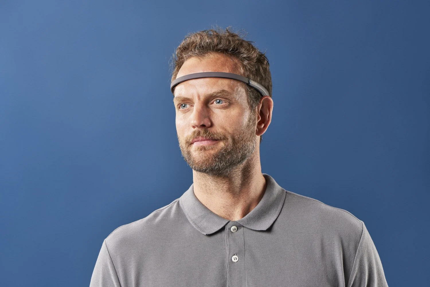 Man in a polo shirt wearing a tech headband wearable, shot against a solid blue background, clean commercial lifestyle portrait with even studio lighting