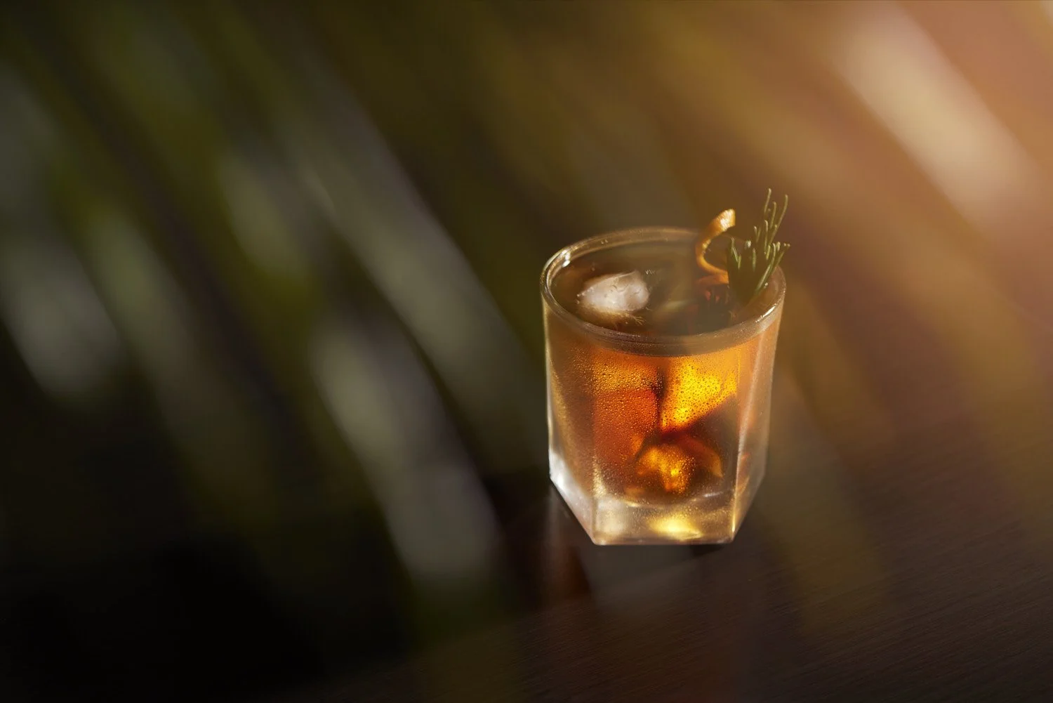 Single amber shot glass filled with whisky or dark spirits, isolated against a dark blurred background with moody low-key directional lighting
