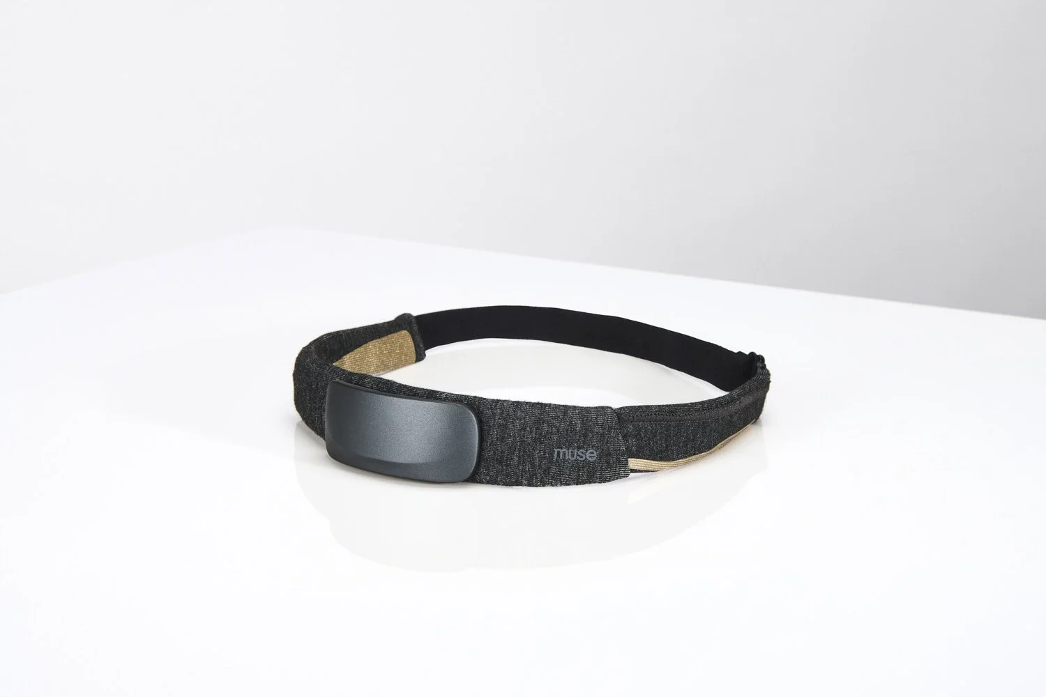Single slim black tech wearable headband device lying flat on a clean white surface, minimalist product shot with soft even studio lighting from above