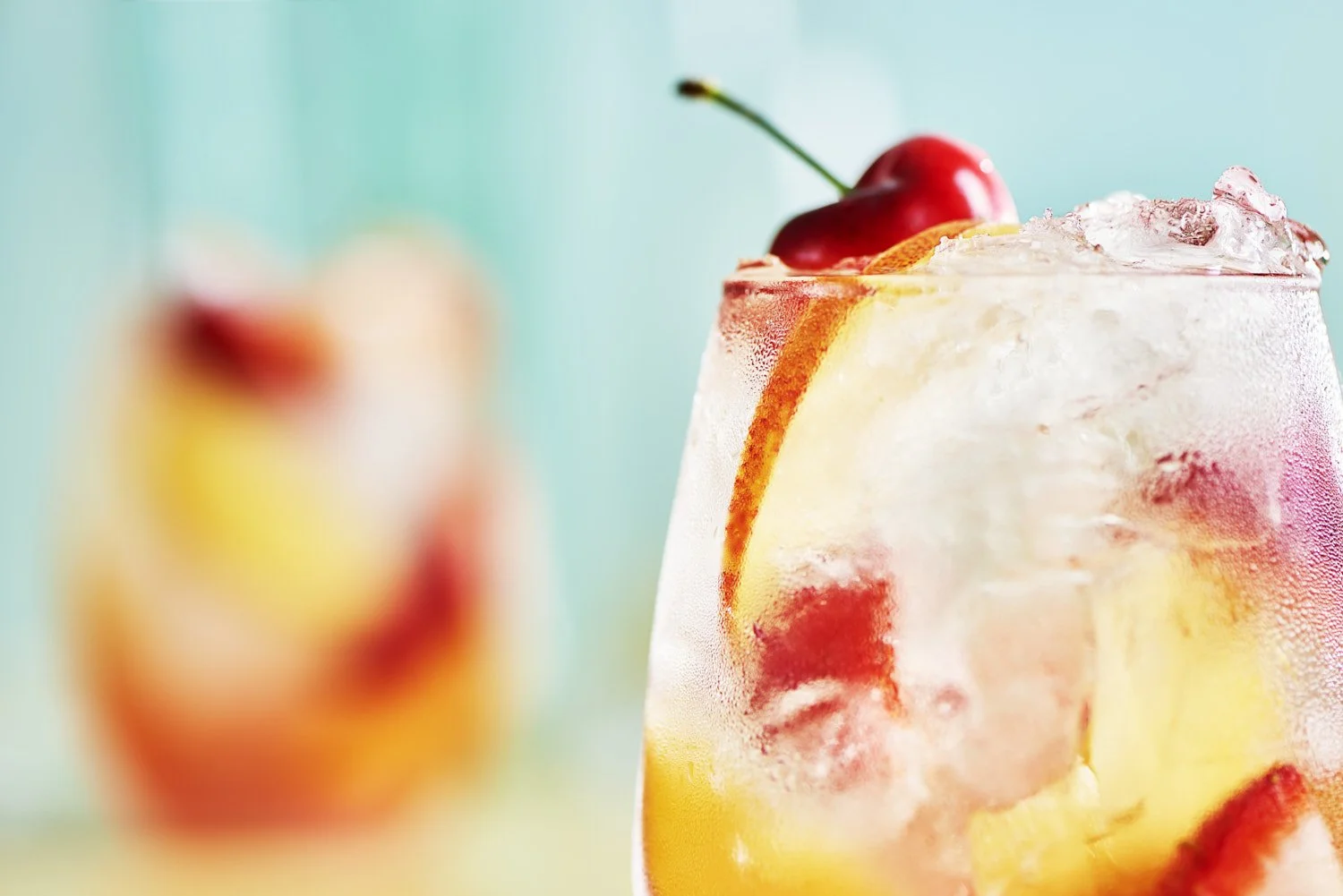Refreshing cherry and citrus cocktail on the rocks in a short glass with a cherry garnish, shot on a soft aqua background with shallow depth of field