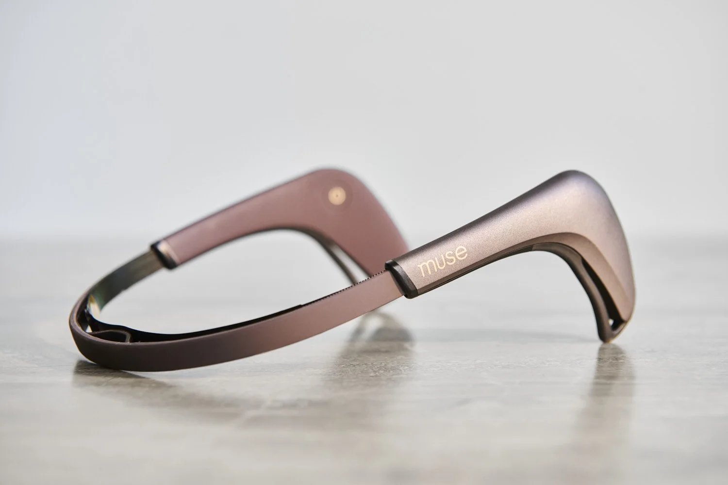 Standalone rose gold and black tech wearable headband device on a clean white surface, elegant product shot with soft directional lighting and subtle shadow detail