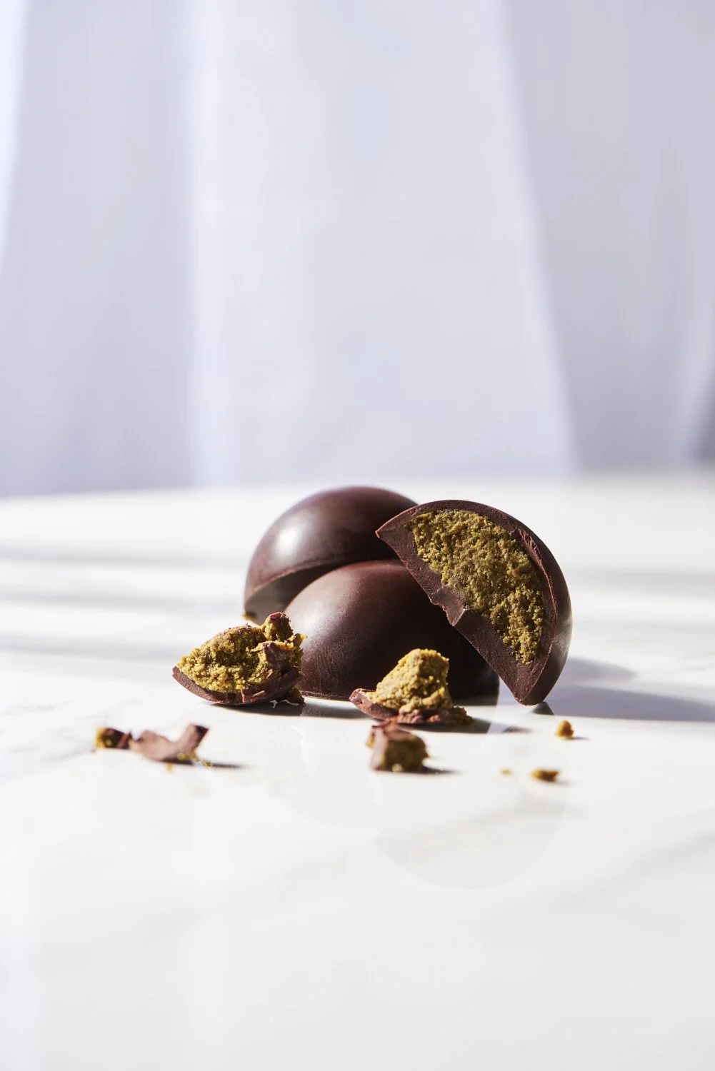 Artistic food or confection product shot of a dark chocolate truffle or bonbon broken open on a clean white surface with scattered crumble detail