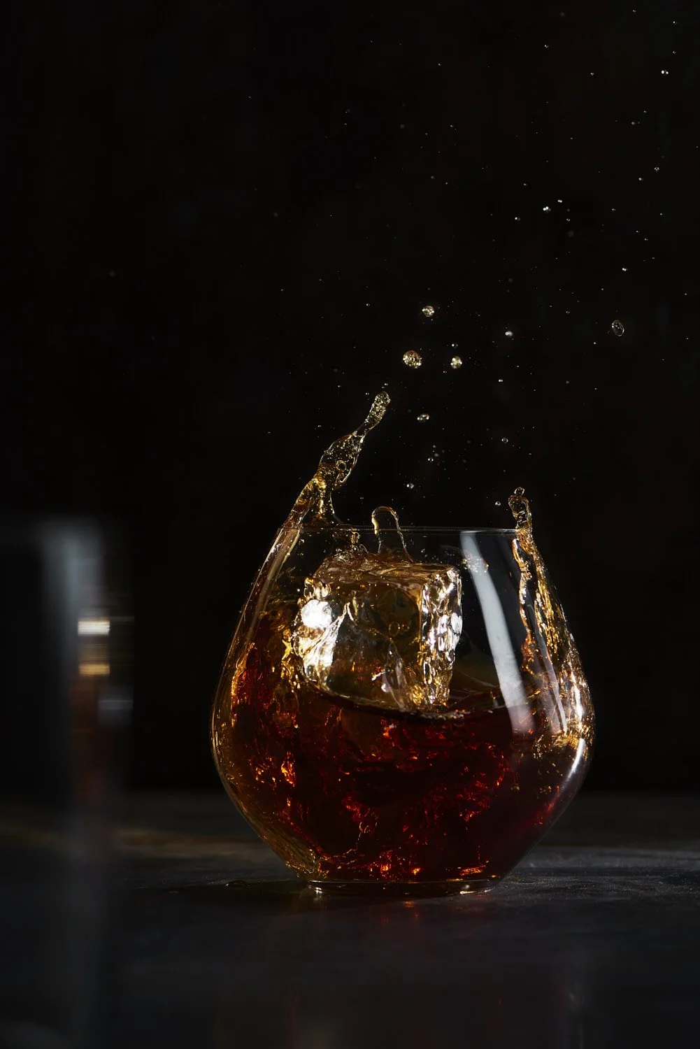 Dark moody studio shot of whiskey being poured into a stemless glass, capturing motion and rich color against a near-black background