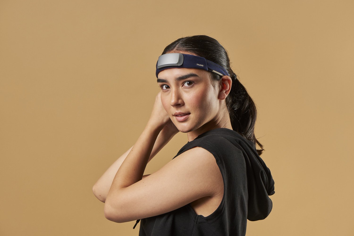 oung woman in profile wearing a sleek black headband wearable device, shot against a warm tan background, clean lifestyle portrait with soft directional light