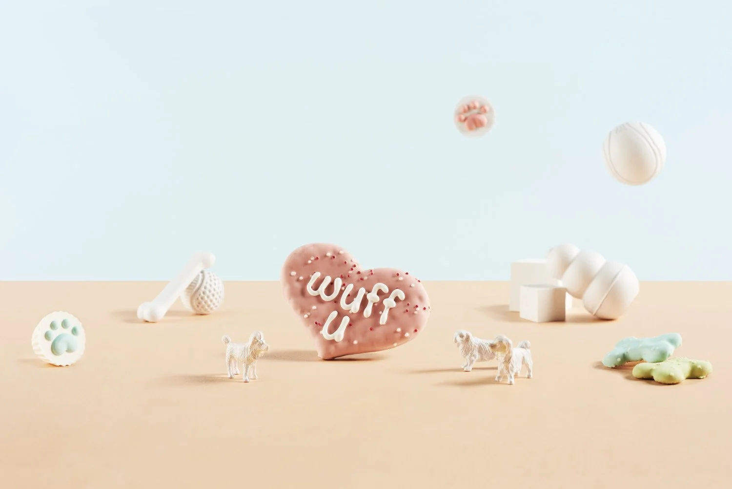 Whimsical miniature desert scene with tiny figures, a cookie or pastry, and a small heart sign arranged on a warm sand-toned surface with pastel blue background