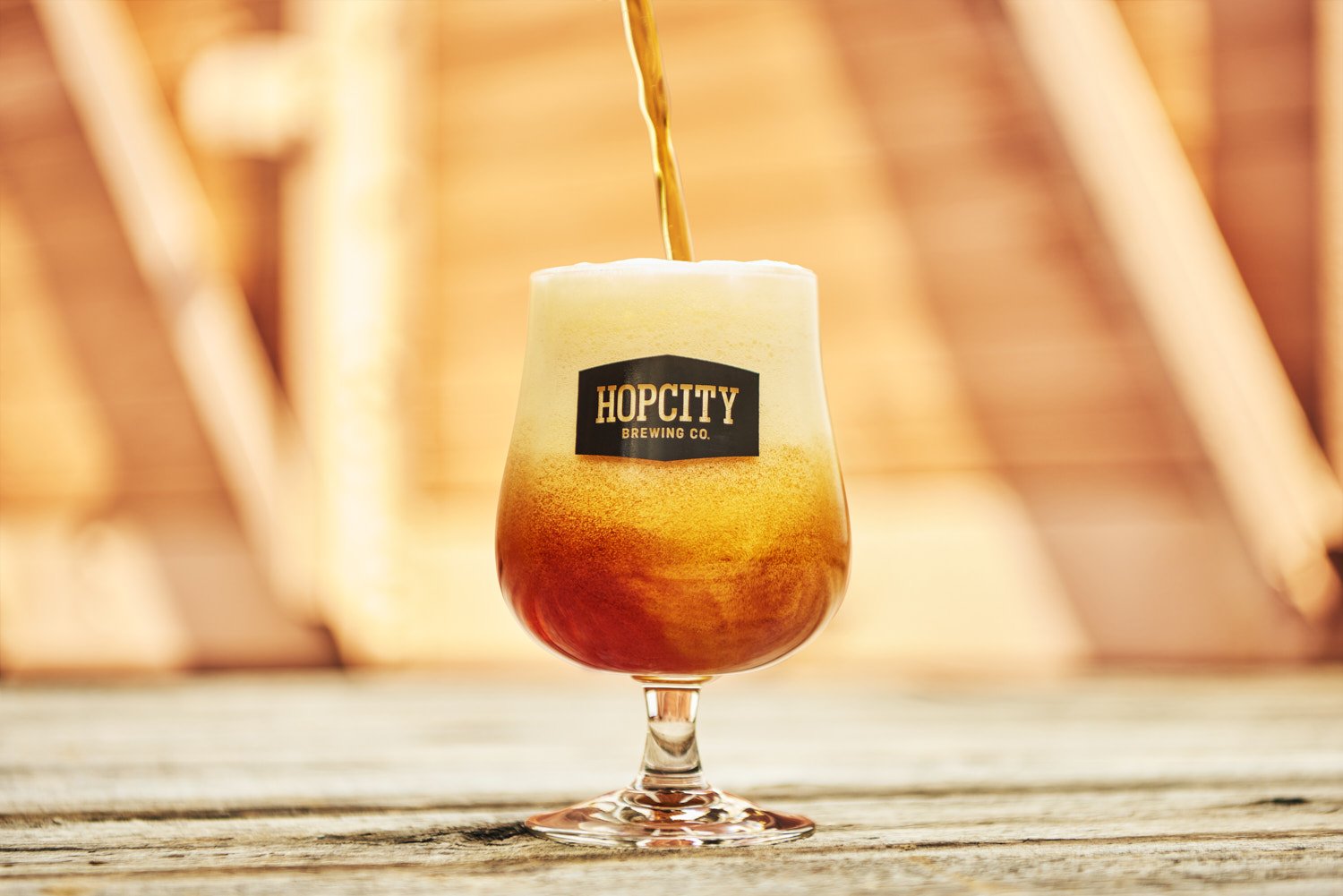 Branded tall cocktail glass filled with an amber drink and garnished with an orange slice, shot in warm golden hour light on a wooden surface