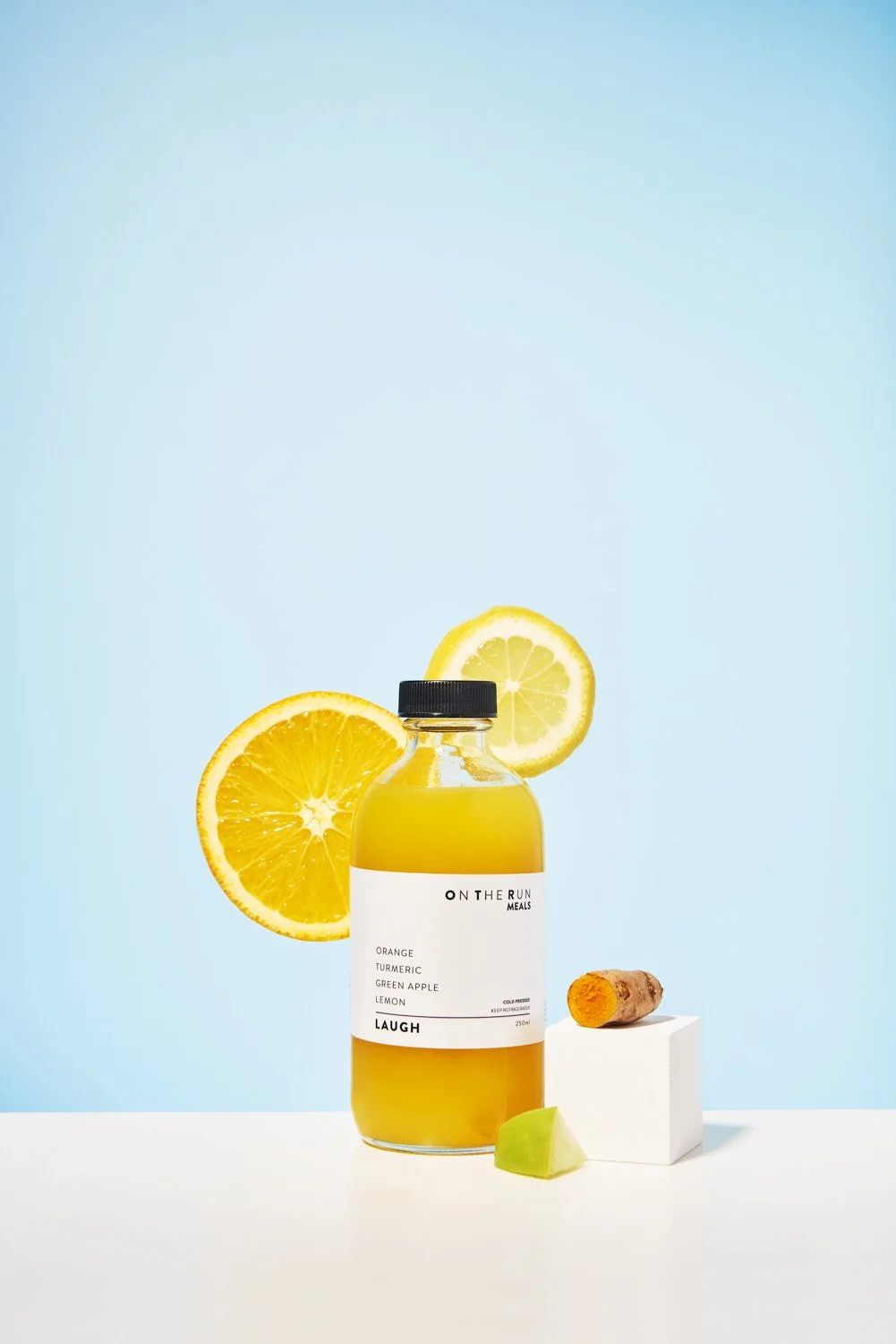 Clean product shot of a juice or beverage bottle with a lemon slice and orange half floating beside it on a soft light blue background