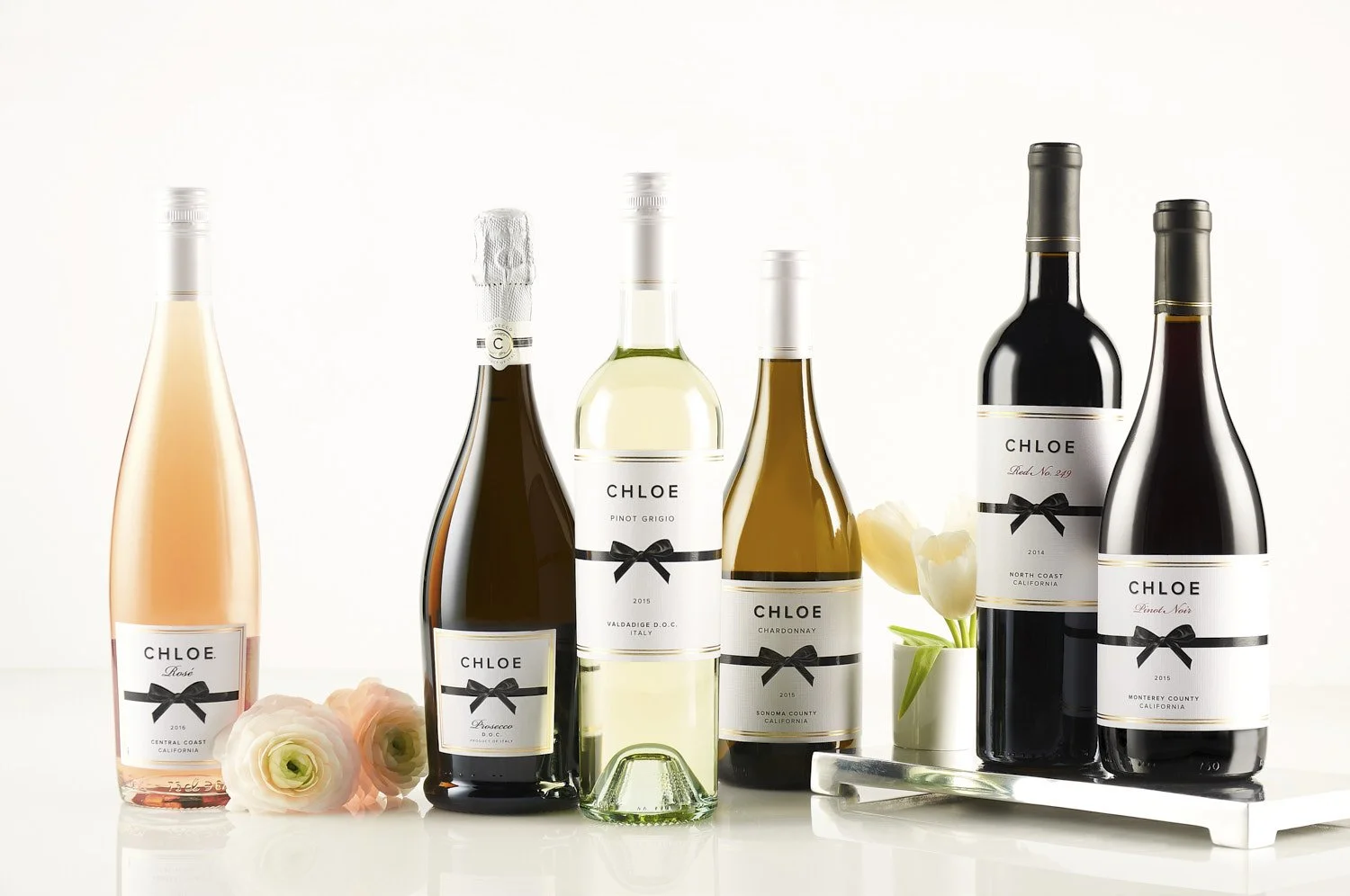 Full lineup of five wine bottles ranging from rosé to white to red, arranged side by side on a white surface with clean studio lighting