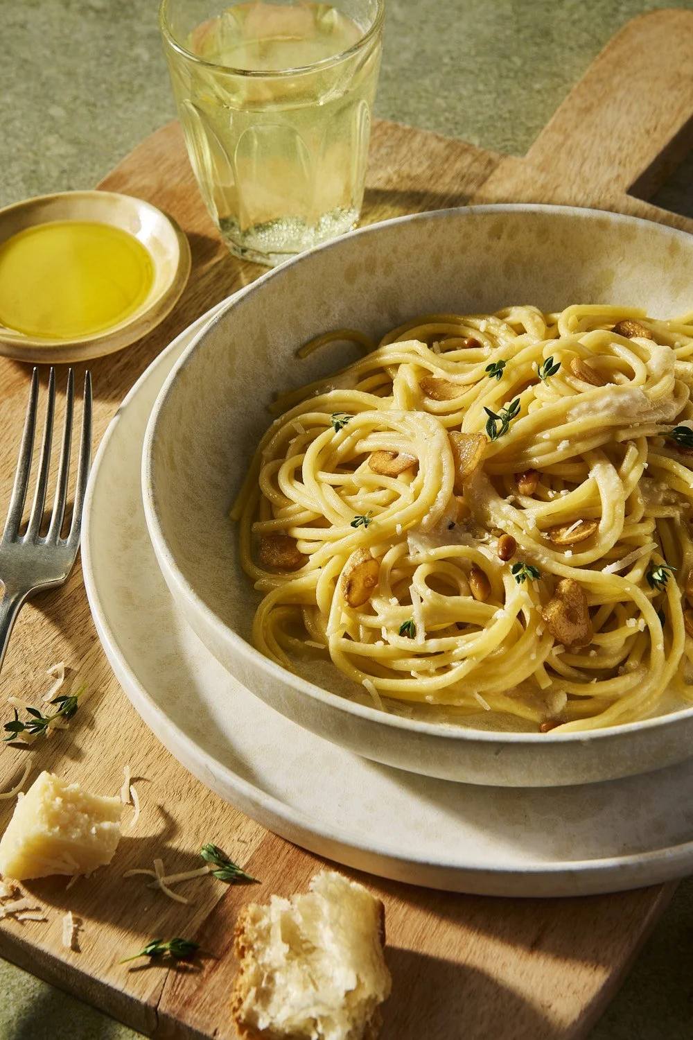 Wide shallow bowl of creamy carbonara-style pasta finished with golden olive oil and fresh herbs, shot with warm side lighting on a soft neutral linen surface