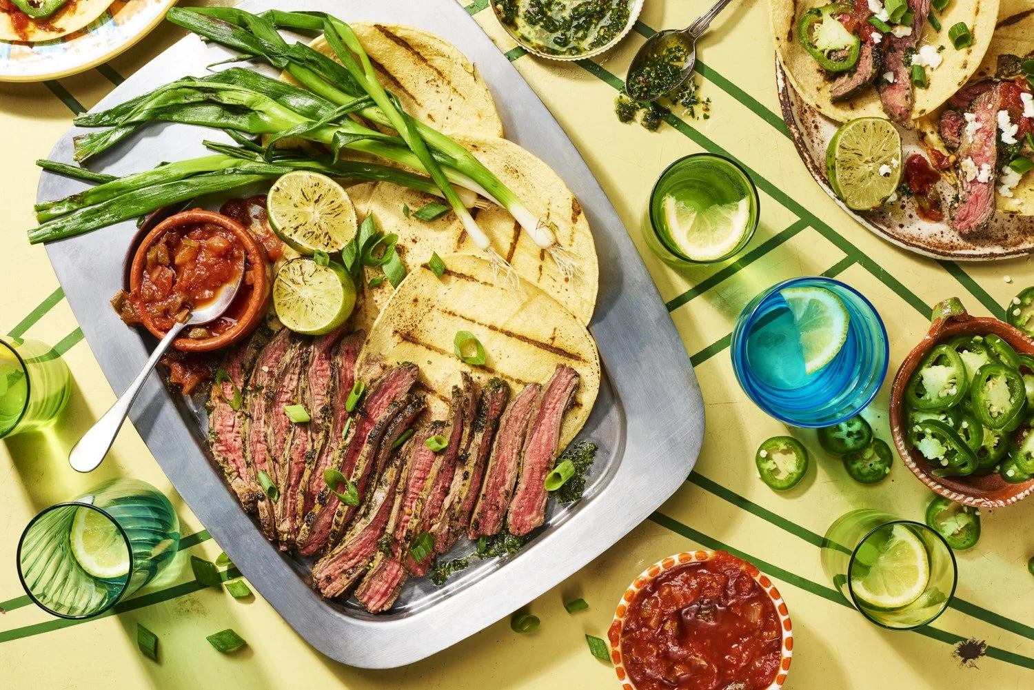 liced grilled flank steak fanned out on a white oval platter alongside roasted cherry tomatoes, green beans, and fresh herbs, shot from a slight angle