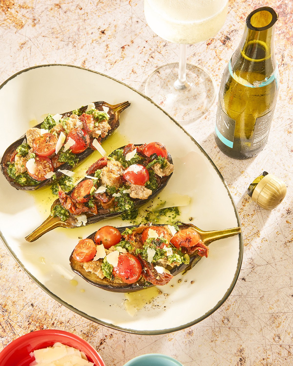 Three loaded stuffed eggplants filled with grains and topped with fresh herbs, microgreens, and colorful garnishes, served on a large white ceramic plate