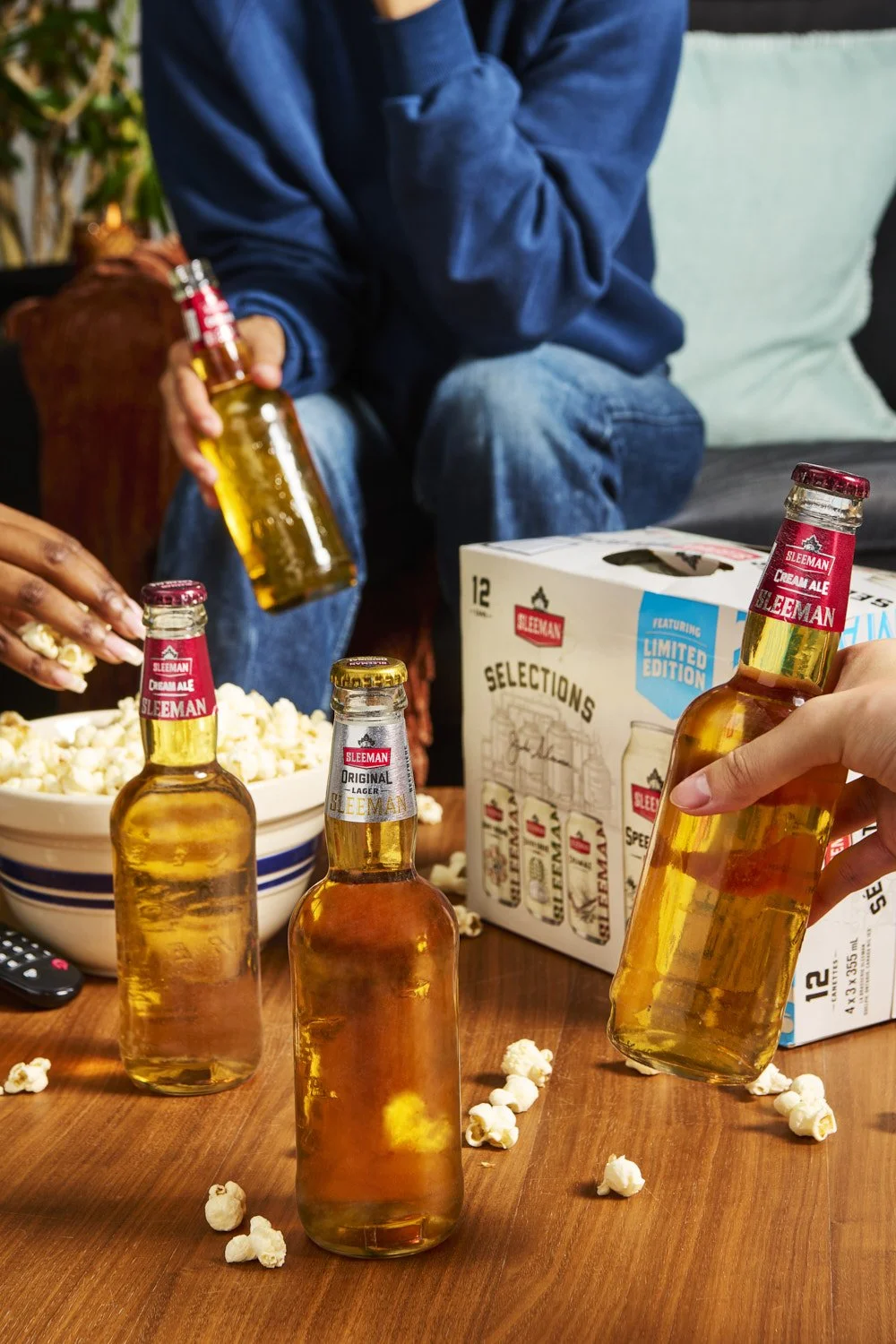 Group of people reaching for whisky bottles and branded beverages on a table, social gathering lifestyle shot with warm ambient lighting