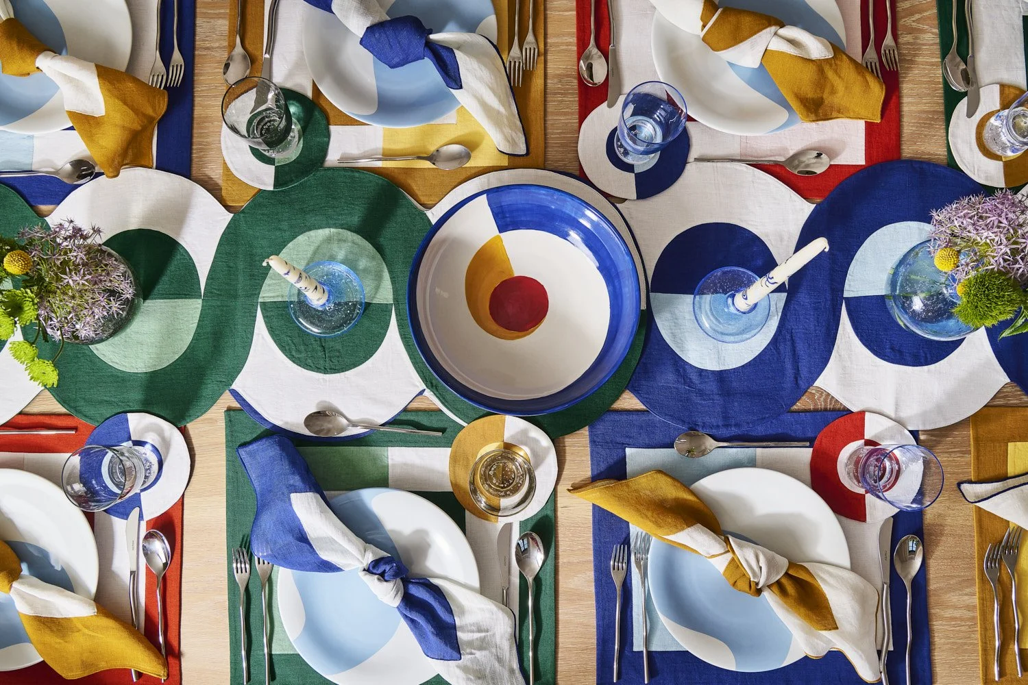 Overhead flat lay of colorful patterned ceramic plates and bowls in blue, green, and red tones, arranged in a dense and vibrant tabletop styling composition