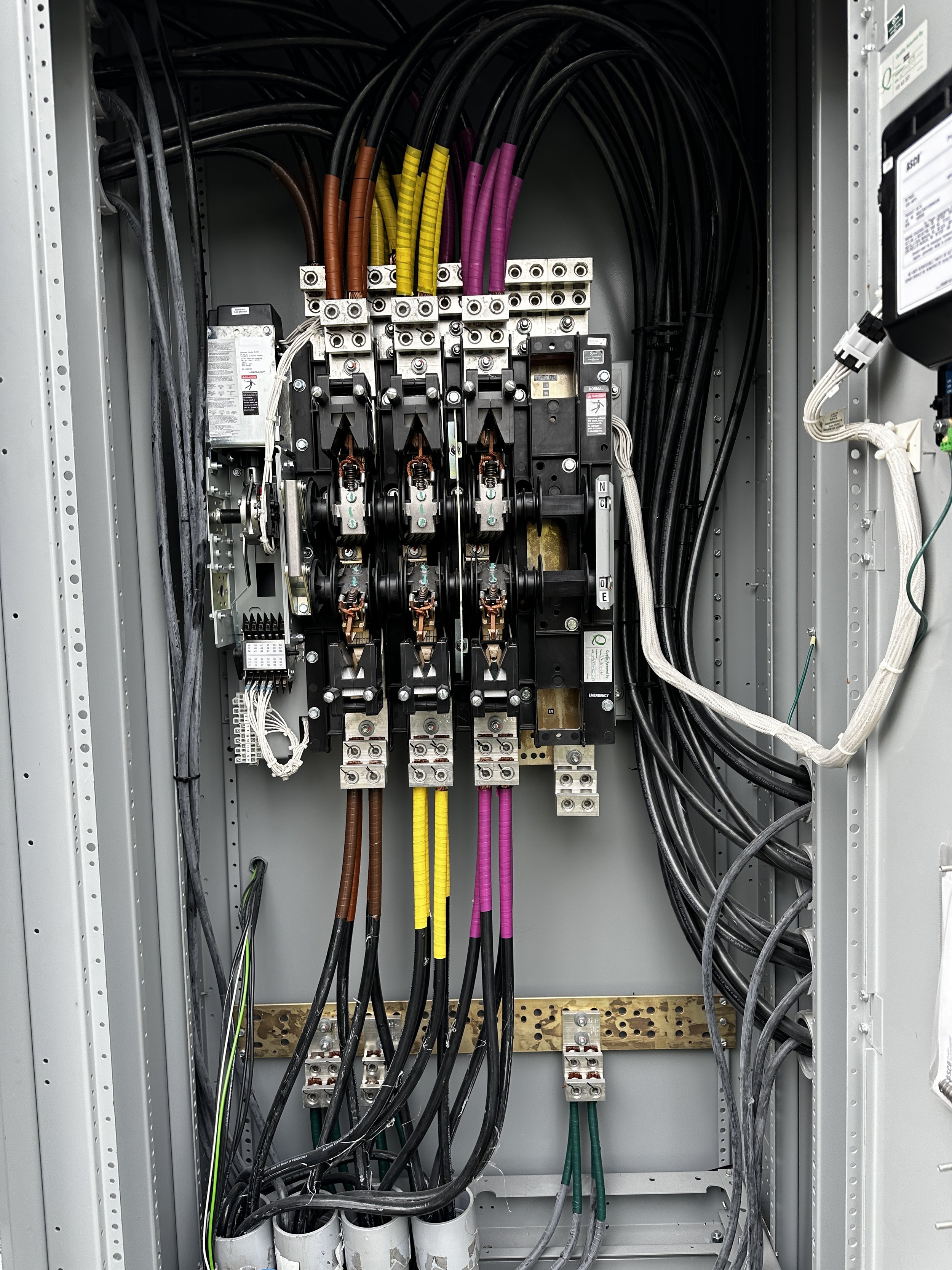 Inside an electrical control panel with various black, brown, yellow, and purple cables connected to circuit breakers and electrical components.