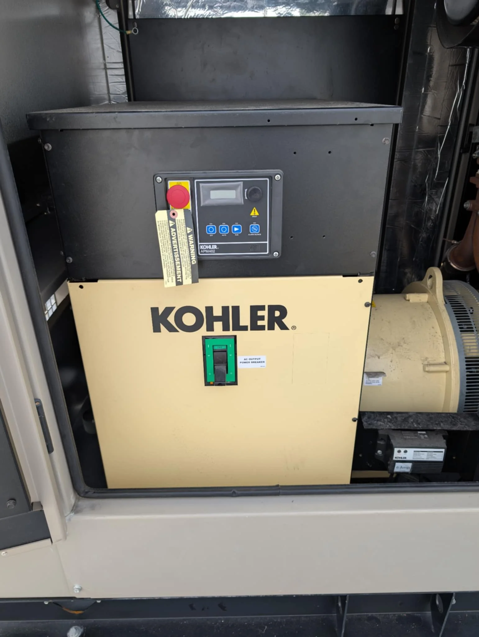 A Kohler generator inside an enclosure with control panel and switch, used for backup power supply.