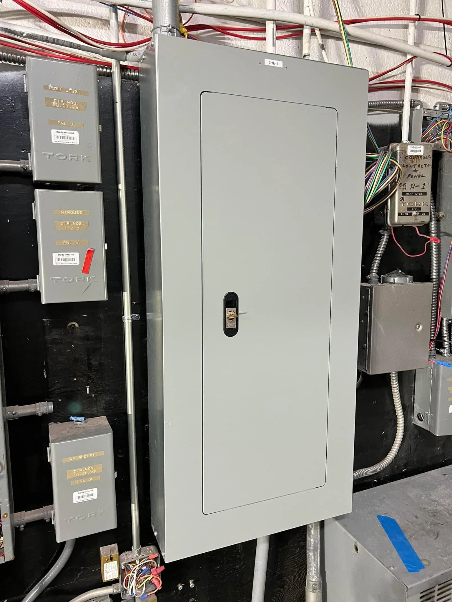 Electrical control panel with multiple smaller boxes, wires, and conduits on a black wall.