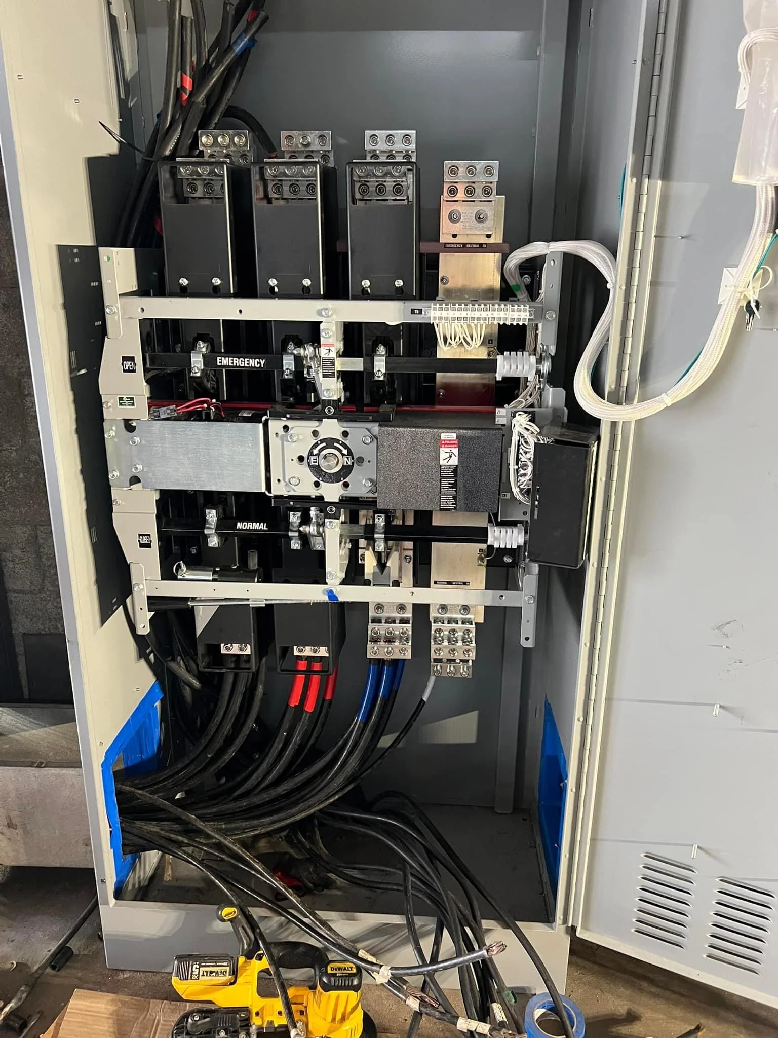 Electrical control panel with various switches, wires, and components inside a metal enclosure, with tools below.