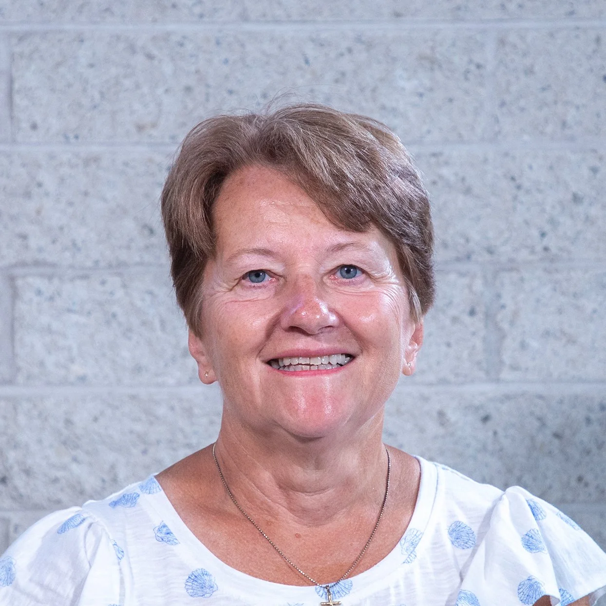 Person smiling in front of a light-colored brick wall.