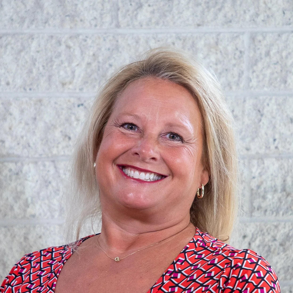 Smiling woman with blonde hair against a light-colored brick wall.
