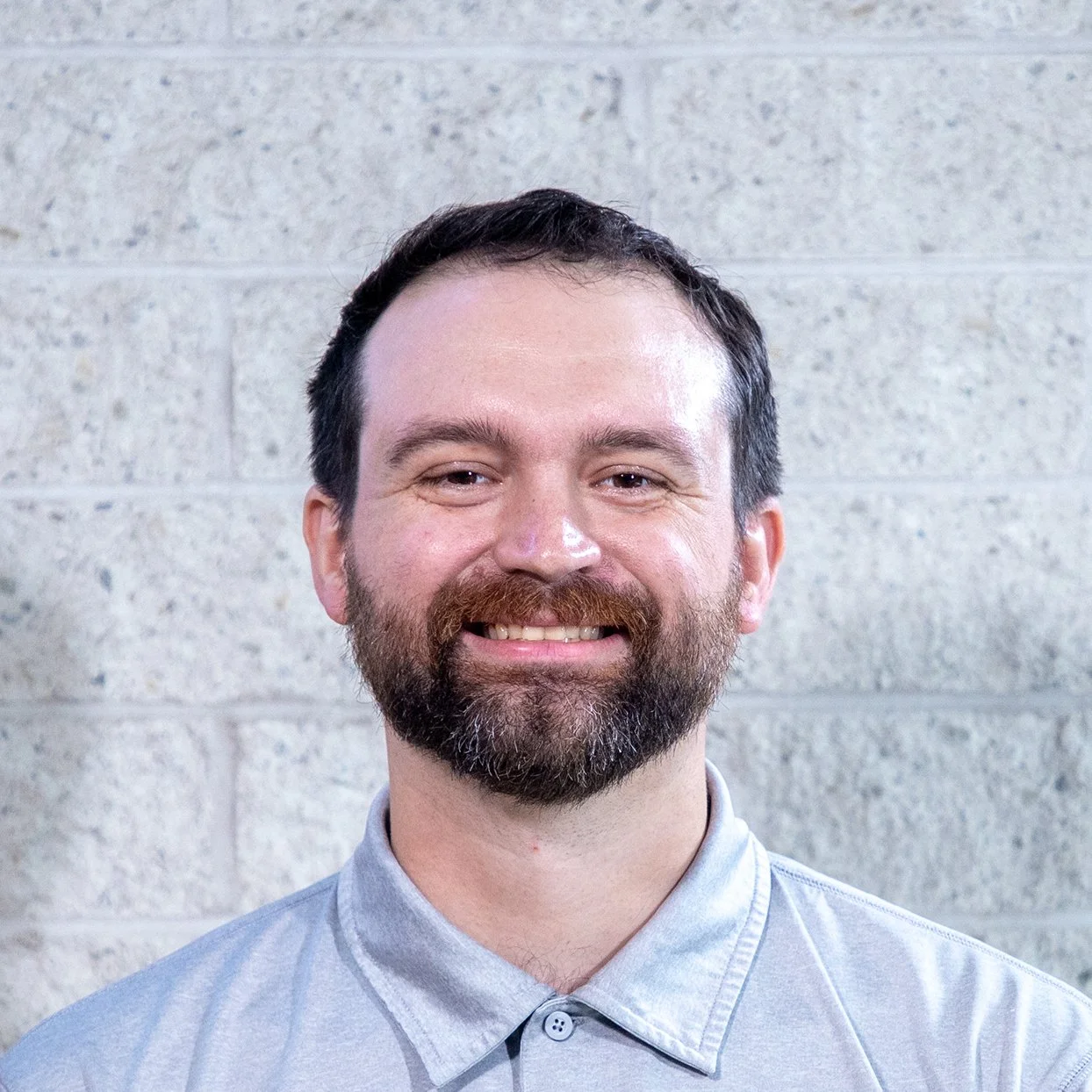 Man smiling in front of a brick wall, wearing a red shirt.