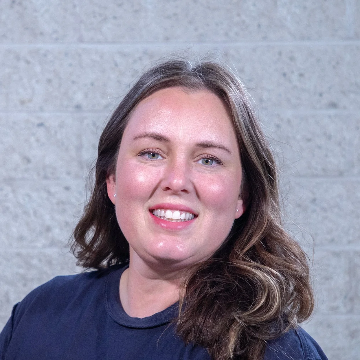 Person with medium-length hair in green jacket against gray brick wall
