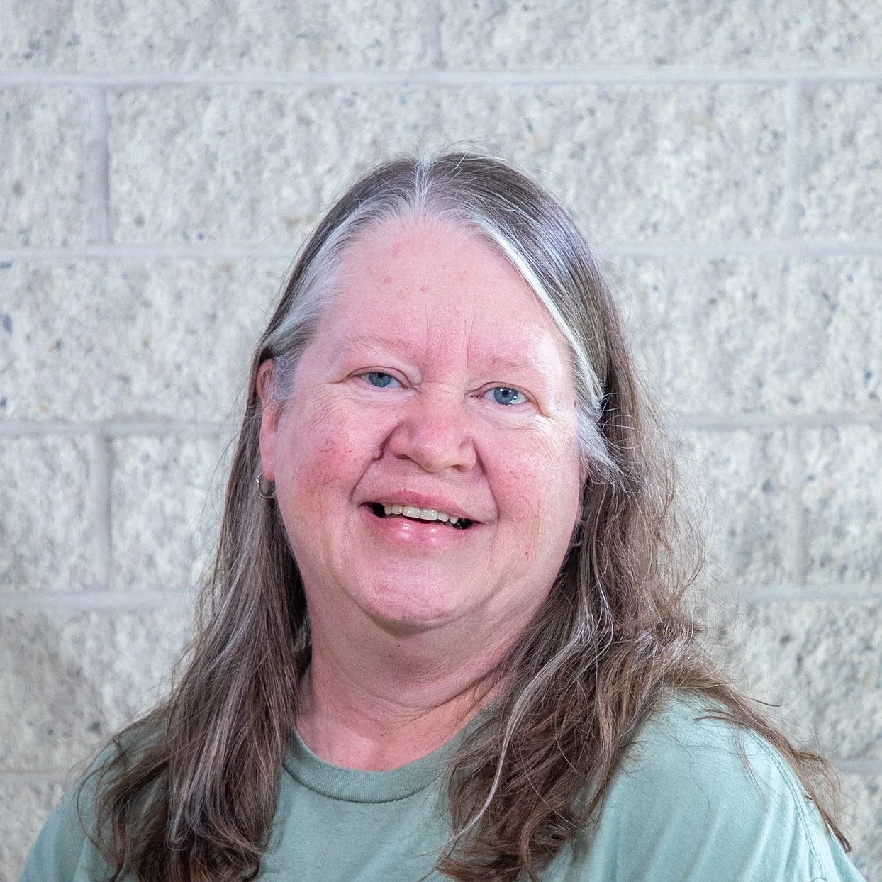 Woman with long hair standing against a textured brick wall.