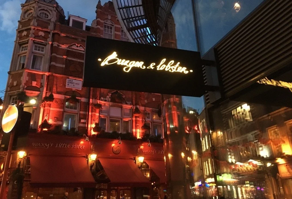 Burger & Lobster restaurant sign with building reflection at night in Leicester Square