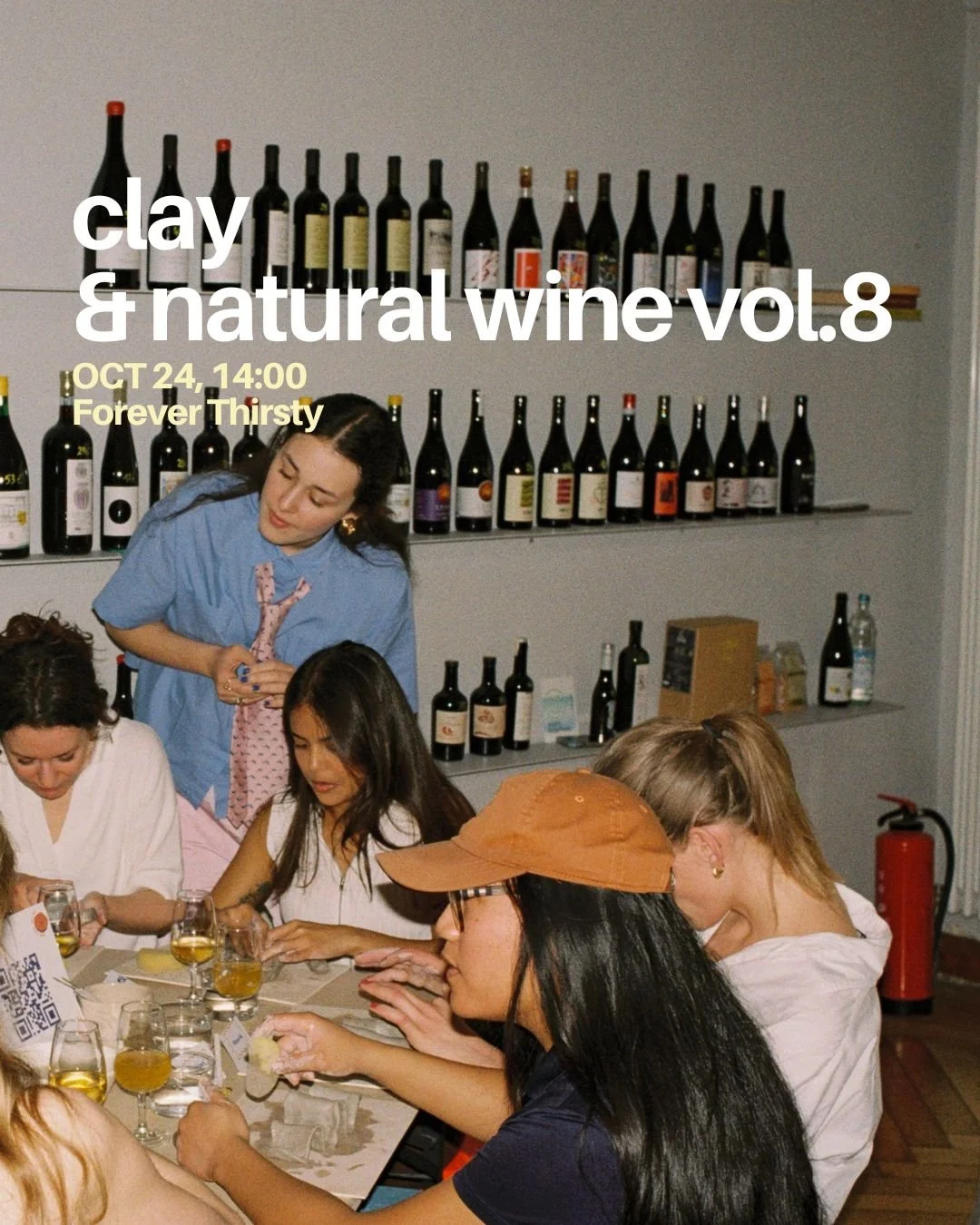 Group of women tasting wine at a wine tasting event with shelves of wine bottles on the wall behind them.