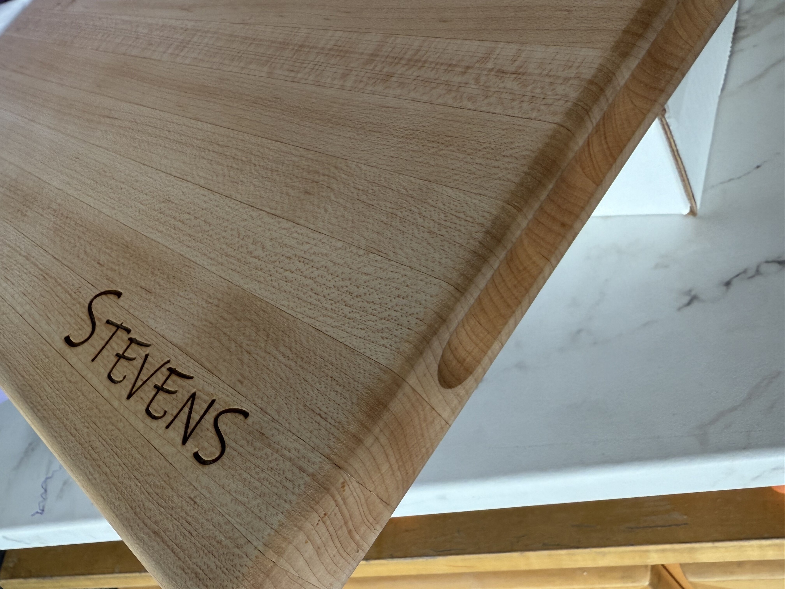 Close-up of a wooden cutting board with the name "STEVENS" engraved on it.