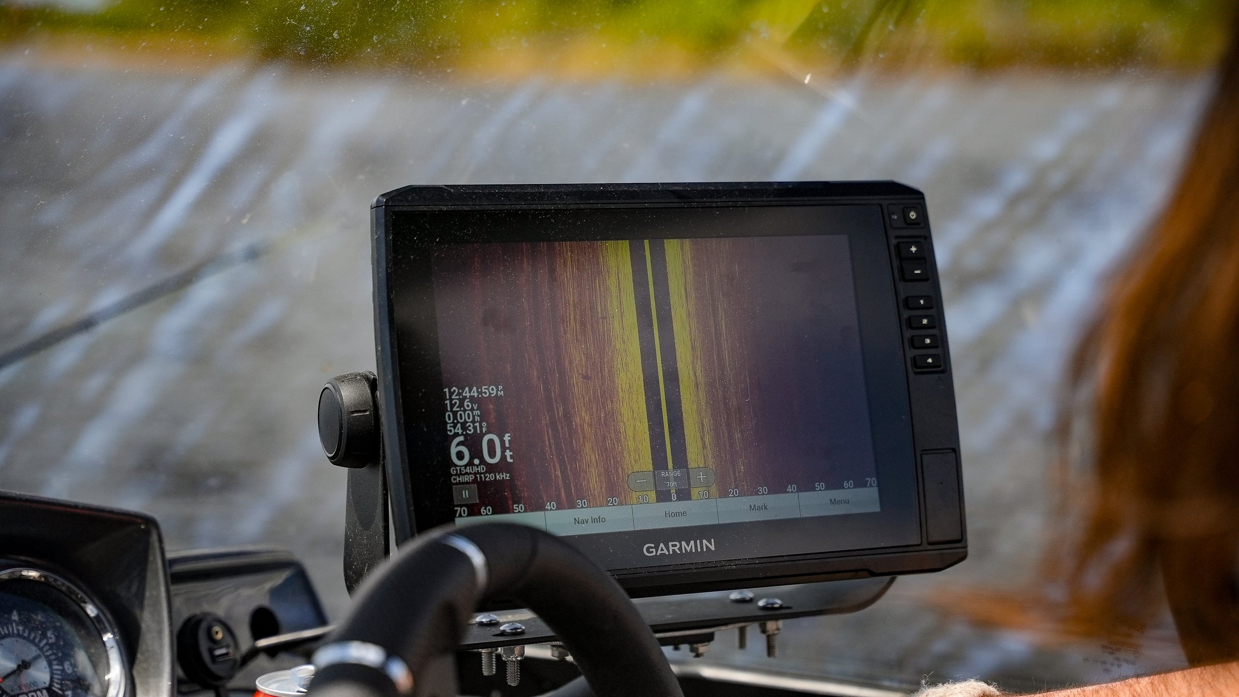 A Garmin fishfinder GPS device mounted on a boat dashboard, showing water depth, temperature, and sonar readings with a background of flowing water.