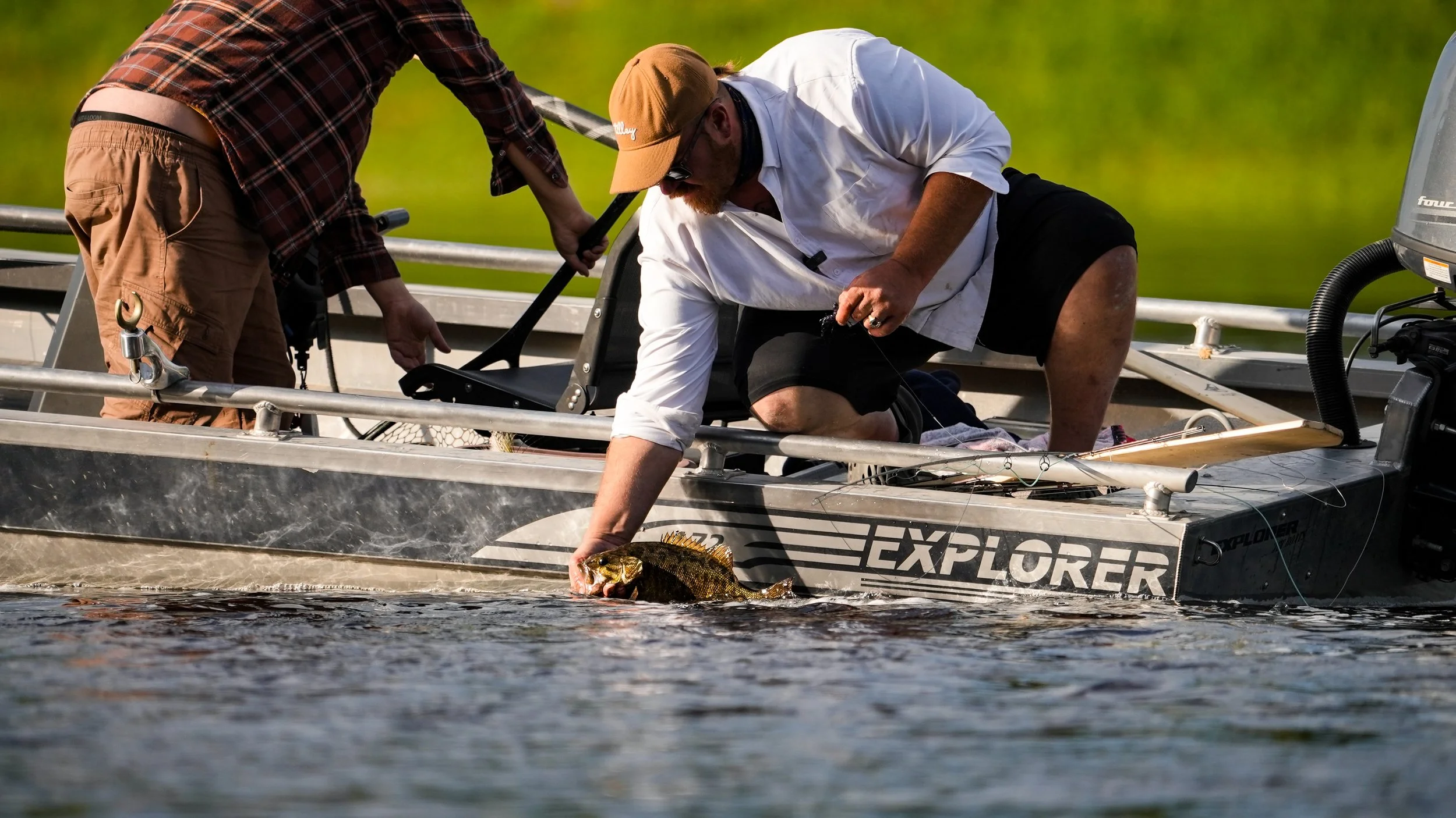 Two men on a boat releasing a fish into the water during daytime.