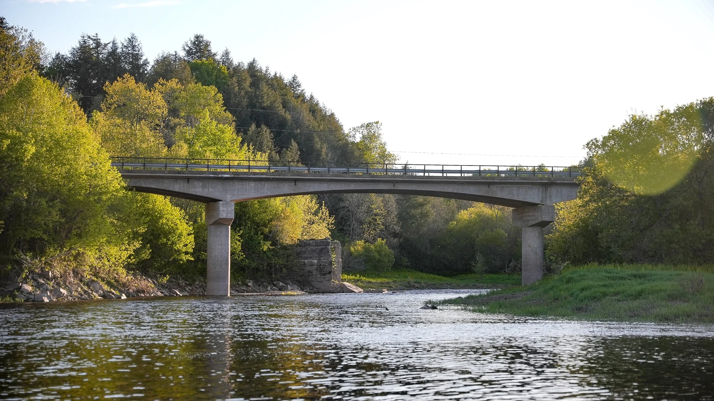 A concrete bridge over a river with green trees on both sides and a clear sky.