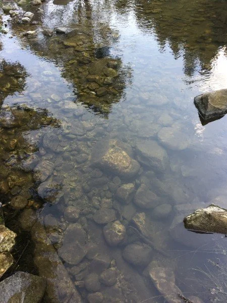 Clear water flowing over river stones, symbolizing reflection, emotional clarity, and the deeper layers beneath the surface.