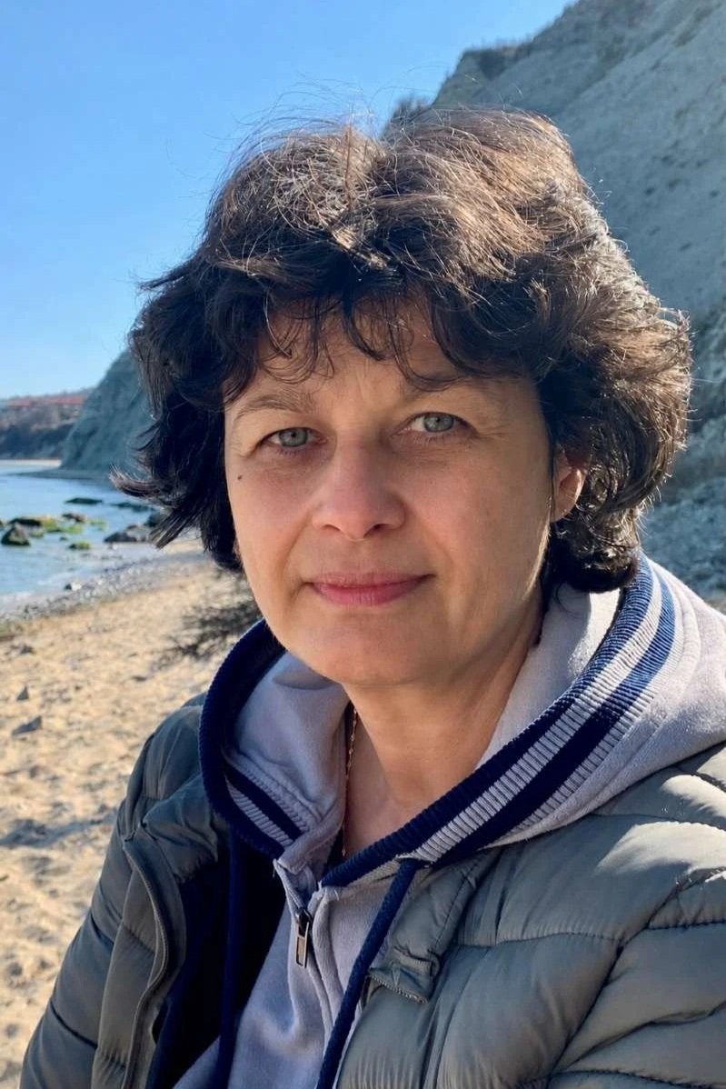 Maria, Reiki Master and energy practitioner, standing outdoors by the sea in natural light.